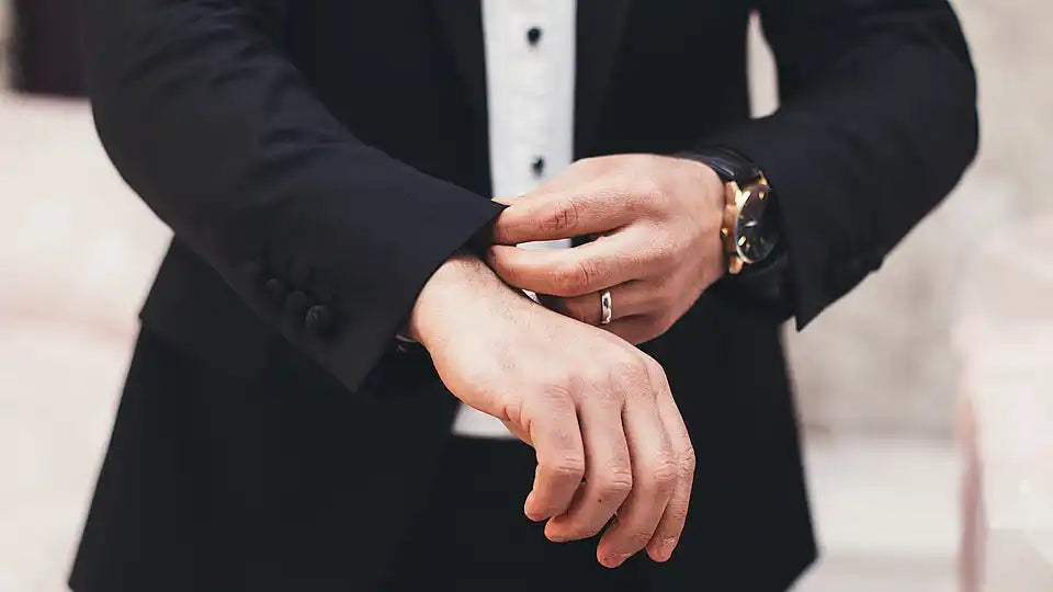 A person in a black suit adjusting their cuff, revealing a watch and a ring.