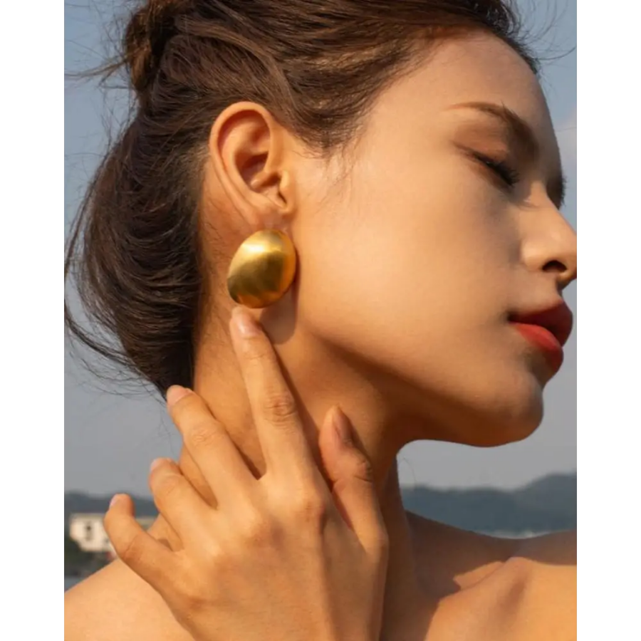 Gold shield earrings worn on ear, showing lightweight fit and matte texture